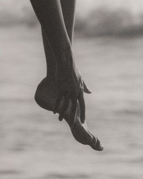 A pointed foot held by a hand over the sea