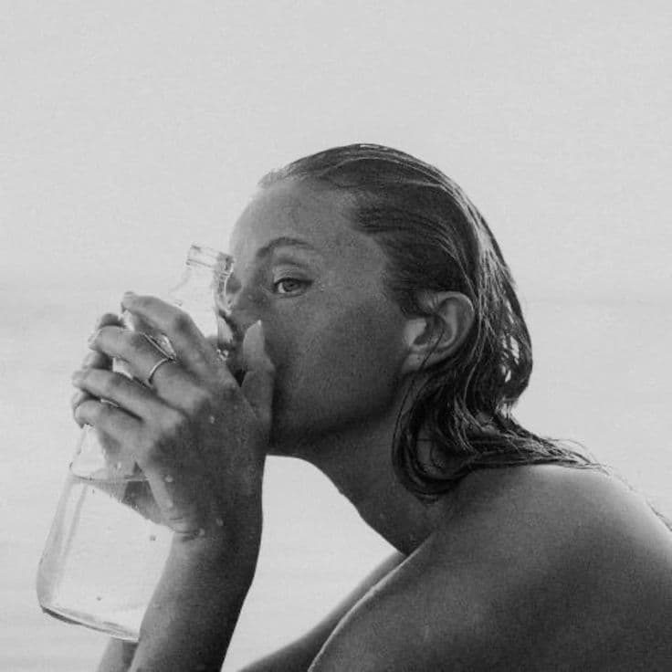 Woman with wet hair drinking from a glass bottle by the sea